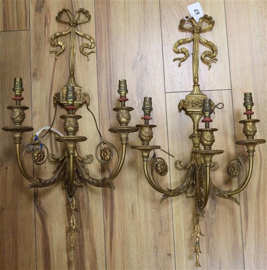 A pair of ormolu three branch wall sconces, decorated with ribbons, rams heads and foliage overall length 59cm